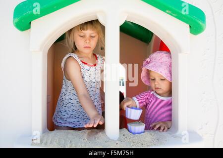 Female toddler and sister playing with sand on playhouse windowsill Stock Photo