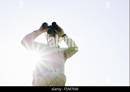 Low angle view of senior man in sunlight looking through binoculars Stock Photo