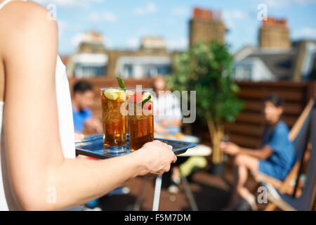 Woman carrying tray of cocktails at rooftop party Stock Photo