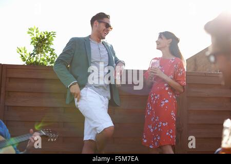 Mid adult couple chatting and drinking at rooftop party Stock Photo