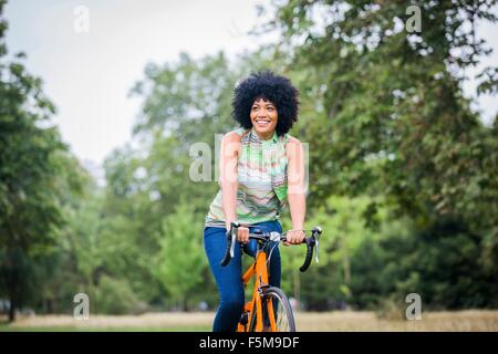 Front view of mature woman with afro riding bicycle looking away smiling