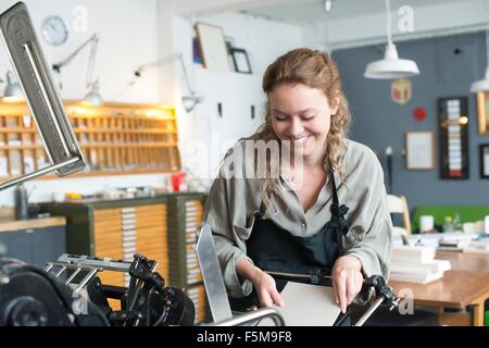 Female printer inserting paper to print machine in workshop Stock Photo