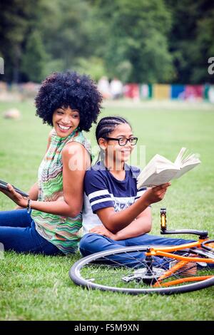Boy and mother back to back in park reading book Stock Photo