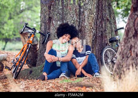 Mature woman and son sitting against park tree Stock Photo