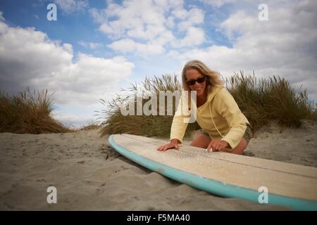 Senior woman on beach, waxing surfboard Stock Photo