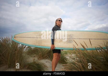 Portrait of senior woman on sand, holding surfboard Stock Photo