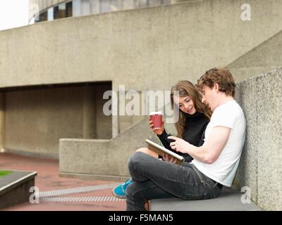 Young couple having coffee, using smartphone on concrete bench, Melbourne, Victoria, Australia Stock Photo