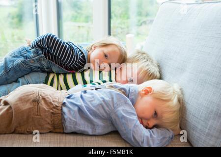 Portrait of tired boy and two toddlers lying on sofa Stock Photo