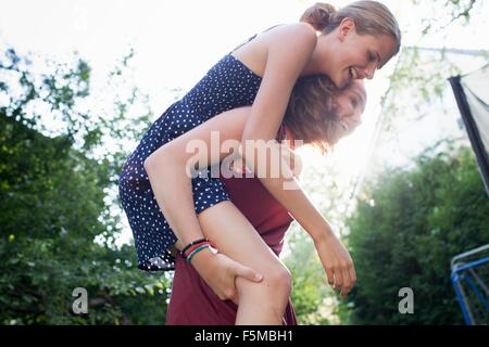 Teenage girl giving best friend a piggy back in park Stock Photo