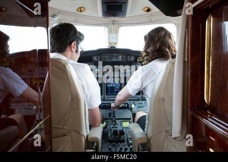 Rear view of male and female pilots in cockpit of private jet Stock Photo