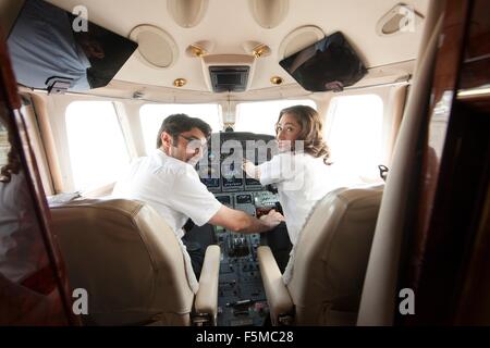 Rear view of male pilot with hand on womans knee in cockpit of private jet Stock Photo
