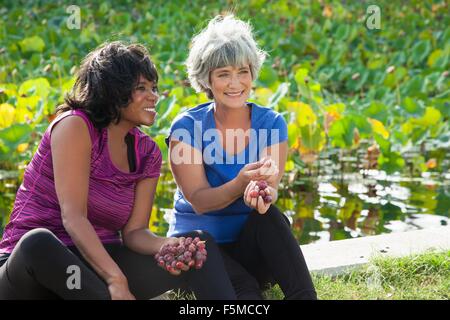 Mature female friends sitting in park, eating grapes Stock Photo
