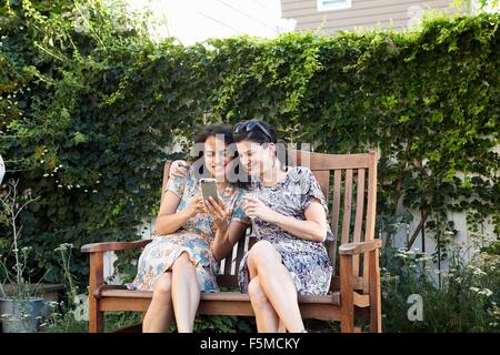 Two women reading smartphone texts on patio Stock Photo