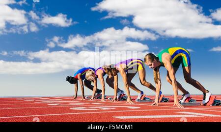 Four female athletes on starting blocks, about to start race Stock Photo