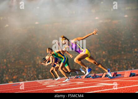 Four female athletes on athletics track, leaving starting blocks Stock Photo