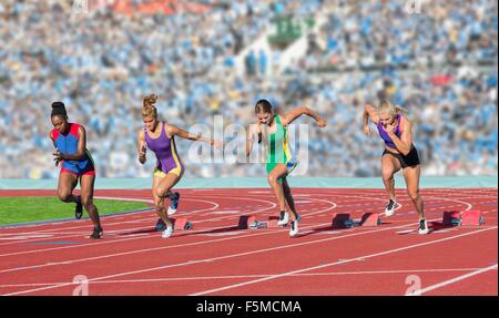 Four female athletes on athletics track, leaving starting blocks Stock Photo