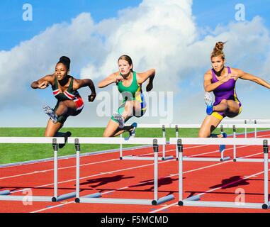 Runners jumping over hurdle on track Stock Photo