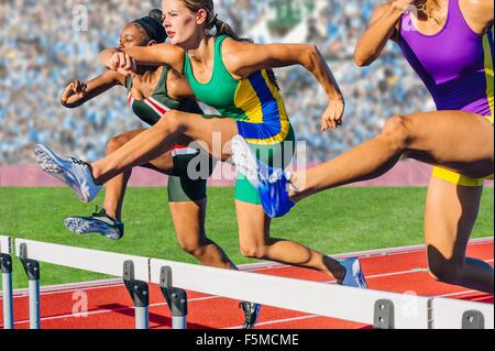 Runners jumping over hurdle on track Stock Photo