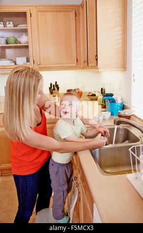 Mother washing son's hands in kitchen sink Stock Photo