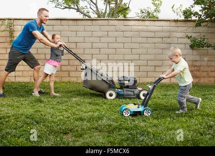 Family mowing lawn in backyard Stock Photo