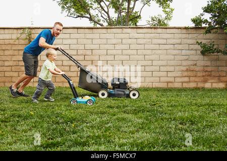 Father and son mowing lawn in backyard Stock Photo