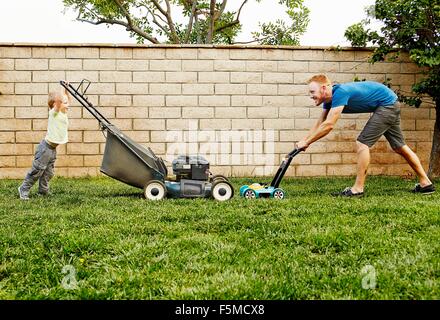 Father and son mowing lawn in backyard Stock Photo