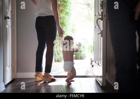 Rear view of mother holding baby boys hands standing at open front door Stock Photo
