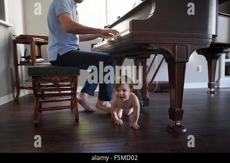 Father playing piano with baby boy crawling at feet Stock Photo