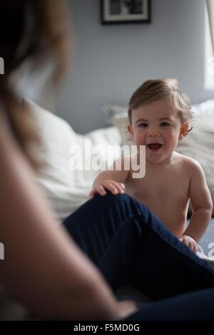 Baby boy holding mothers leg looking at camera smiling Stock Photo