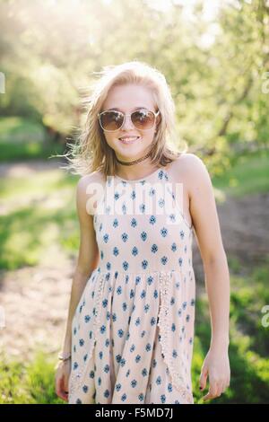 Young woman wearing sleeveless dress and sunglasses looking at camera smiling Stock Photo