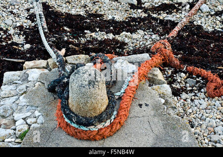 orange and white mooring ropes tethered around stone bollard Stock Photo