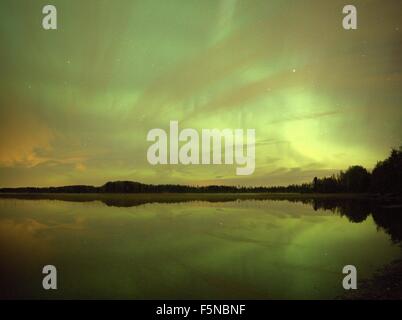 Northern lights (Aurora Borealis) in the night sky over a beautiful lake in Finland. Vibrant green colors on the sky and reflect Stock Photo