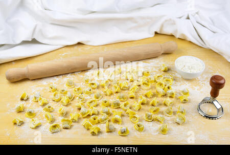 Tortellini emiliani homemade italian raw pasta stuffed with beef and pork meat, rolling pin, flour in a cup and on a wooden back Stock Photo