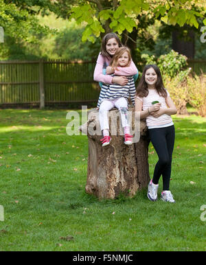 Three Sisters Together. Three young girls, sisters, pose for the camera about a big log. Stock Photo