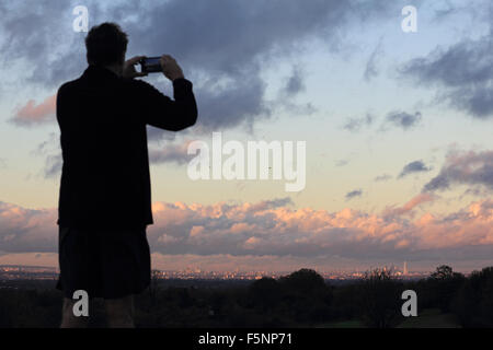 Epsom Downs, Surrey. 7th November 2015. Man takes video of the London skyline from Epsom Downs. After a day of wind and rain the storm finally passed just before dusk, with the sun casting a warm glow over the city of London, as viewed from Epsom Downs. Credit:  Julia Gavin UK/Alamy Live News Stock Photo
