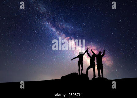 Milky Way. Night sky with stars and silhouette of a happy family with raised-up arms Stock Photo