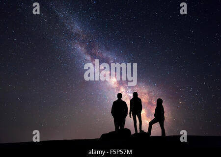 Milky Way. Night sky with stars and silhouette of a happy family with raised-up arms Stock Photo