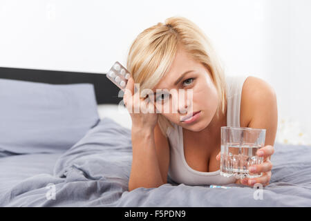 sick woman with pack of pills lying on bed Stock Photo