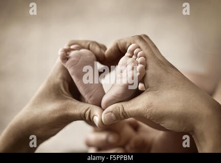 Closeup of mother hands holding cute tiny baby feet, showing baby