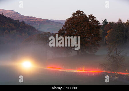 Valley mist over the Langdale Valley at Clappersgate, near Ambleside, in the Lake District, UK with cars driving through the mist. Stock Photo