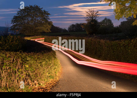 light trails from a car traveling along a country road at night, using a slow shutter speed for a long exposure Stock Photo