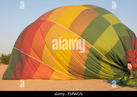 Multi-colored hot air balloon being deflated after landed on a desert ground Stock Photo