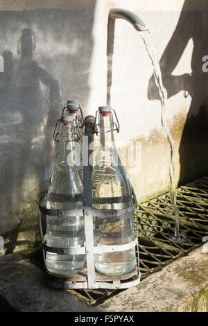 Vintage bottles being refilled by local at water outlet at Alet les Bains springs.Therapeutic qualities, fresh free natural eau. Stock Photo