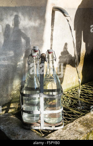 Vintage bottles being refilled by local at water outlet at Alet les Bains springs.Therapeutic qualities, fresh free natural eau. Stock Photo