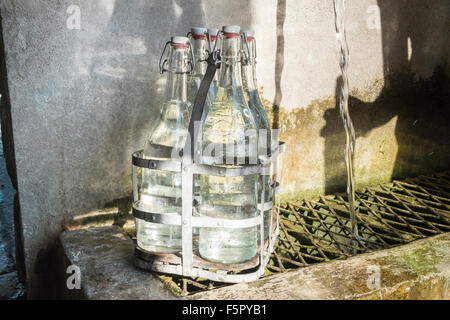 Vintage bottles being refilled by local at water outlet at Alet les Bains springs.Therapeutic qualities, fresh free natural eau. Stock Photo