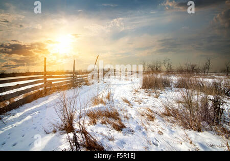Wooden fence in winter field at sunset Stock Photo