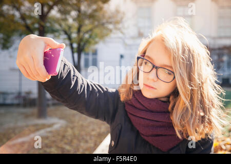 Beautiful Caucasian blond teenage girl taking photo on her smartphone in autumnal park, selective focus on hand with phone, shal Stock Photo