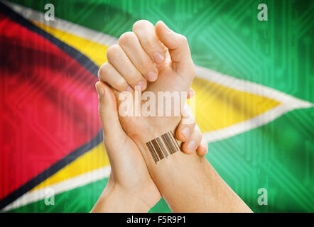 Barcode ID number on wrist of a human and national flag on background - Guyana Stock Photo