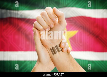 Barcode ID number on wrist of a human and national flag on background - Suriname Stock Photo