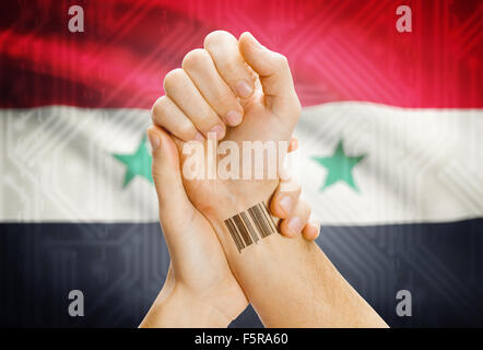Barcode ID number on wrist of a human and national flag on background - Syria Stock Photo